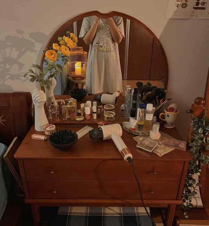 Warm wood tone powder room featuring a large wooden vanity with arch mirror, assorted makeup products and a hair dryer creating a cozy atmosphere