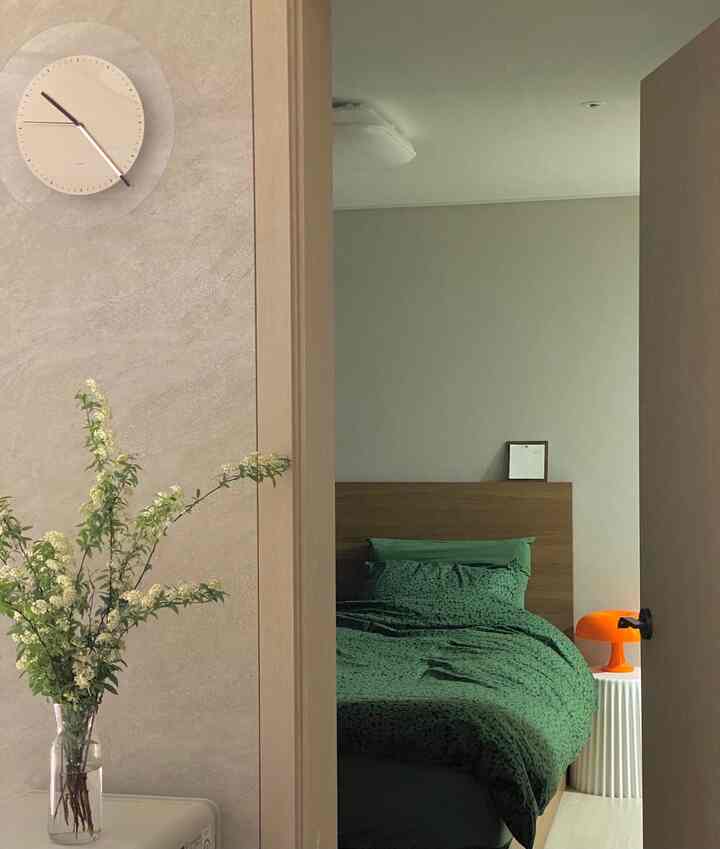 Bedroom in wood tone and white hues featuring green bedding and an orange table lamp, simple and tidy atmosphere
