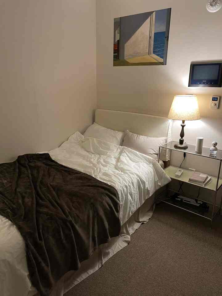 White and brown toned single bedroom featuring a neat bed, nightstand with warm lamp, epitomizing a hotel-like cozy room