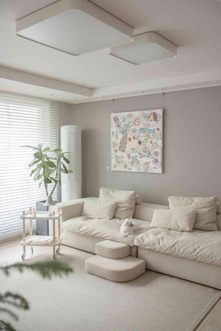 ベージュのファブリックソファとかわいい犬がいるナチュラルトーンのリビング、壁には笑顔あふれる動物のアートが飾られた印象的な空間