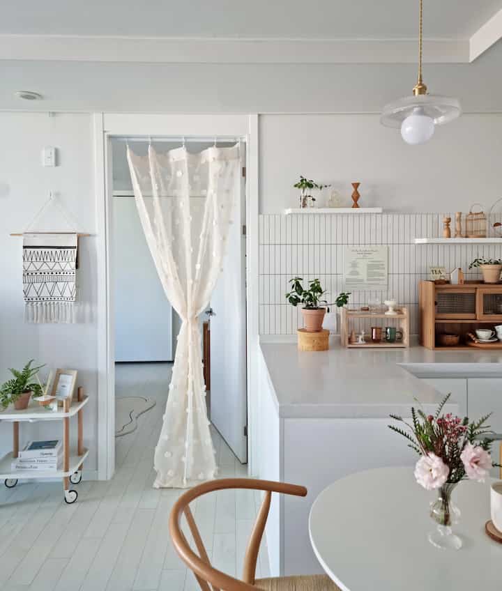 White and wood tone kitchen space featuring a clean dining table and plants, with a natural modern interior
