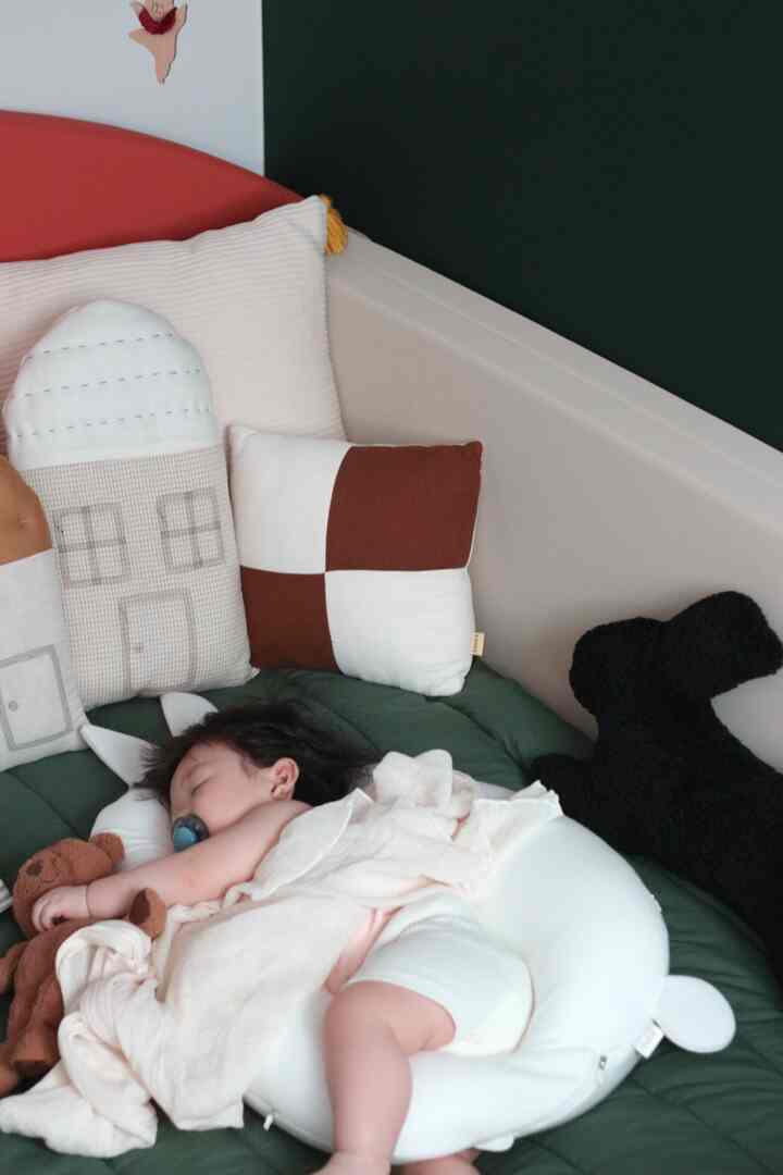白と緑のトーンの子供部屋、クッションと寝具の上で眠る赤ちゃんがいる雰囲気のあるインテリア
