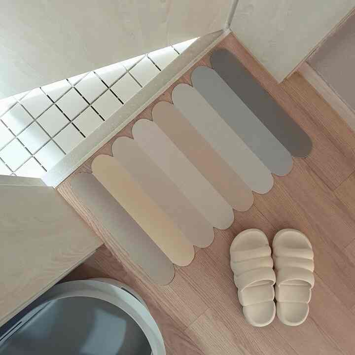 Natural wood tone flooring with a beige and gray bath mat and cream slippers placed in a neat entrance area