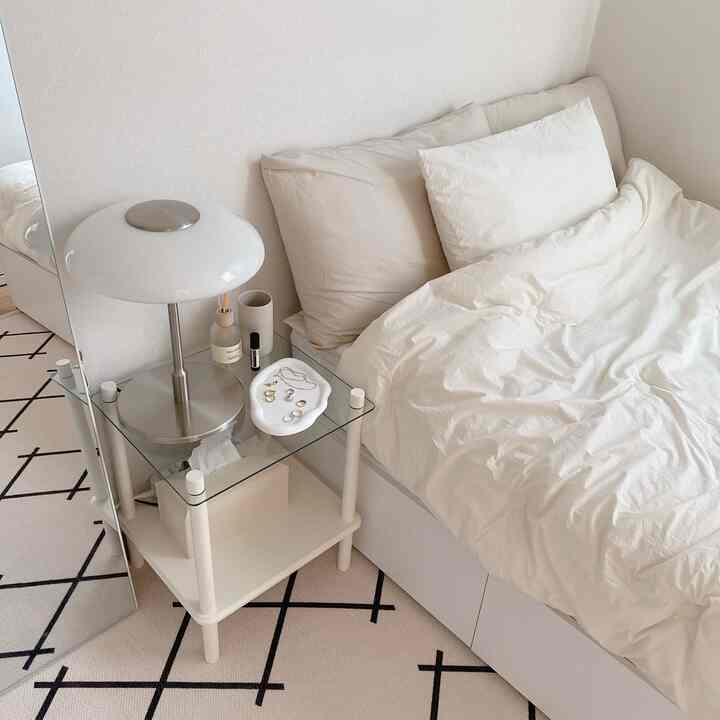 A simple and modern bedroom in white and beige tones featuring a bed, nightstand with table lamp