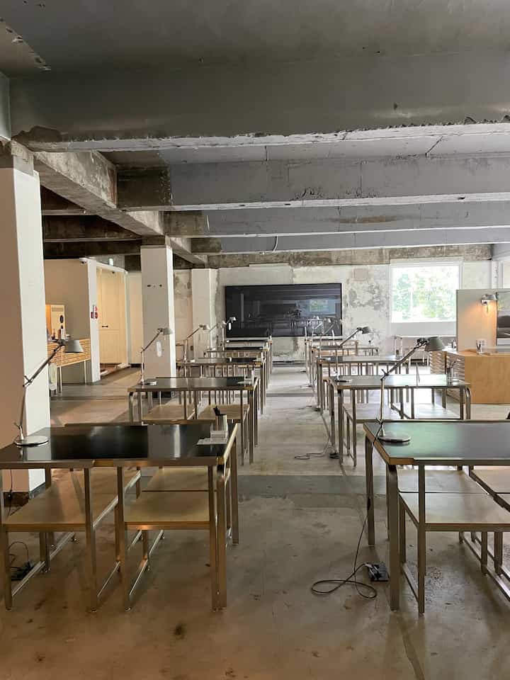 グレー調のインダストリアルなカフェ風空間、スチールと木目調のテーブルにアルテミデのテーブルランプが配されたワークスペース