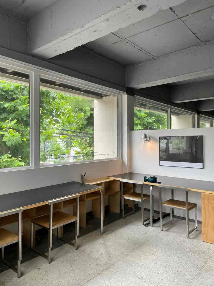 Modern cafe style space with white and wood tones, featuring desks and chairs with large windows providing light and openness