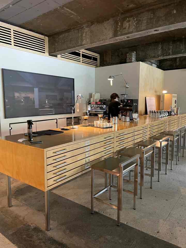 ナチュラルな色調のカフェ風キッチンスペース、大型キッチンアイランドと金属製のブラケットライトが配置された落ち着いた雰囲気のインテリア