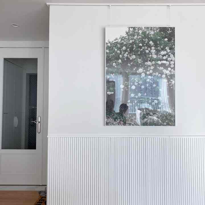 Bright white-toned wall with a large floral art picture frame hung centrally in a minimalistic space