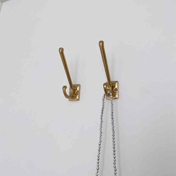 Minimalist white wall with two gold vintage hooks mounted, the right hook holding a crystal-like decoration, accentuating a vintage aesthetic