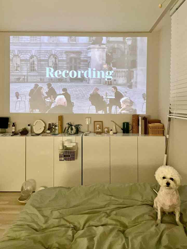 Cozy bedroom with white cabinets and green bedding, projector screen displayed on the wall