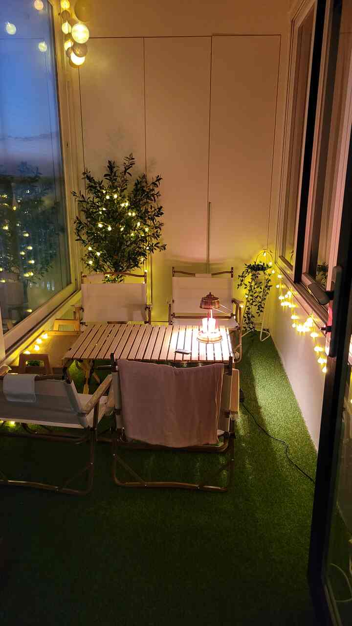 Veranda home camping space with artificial grass, wooden furniture, and warm yellow string lighting
