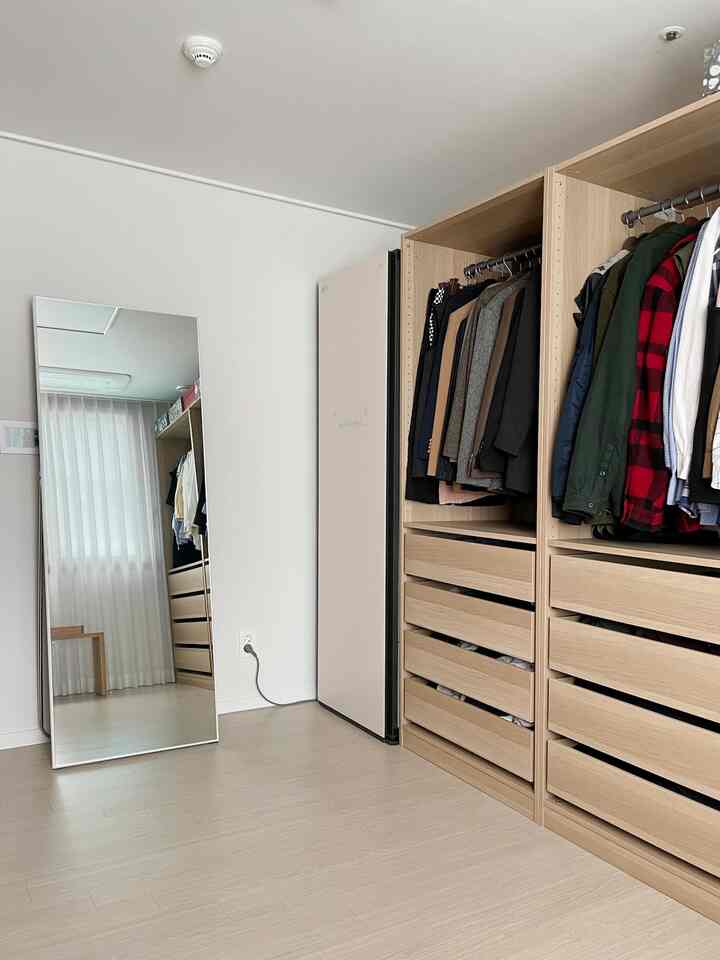 Clean walk-in closet with white and wood tones, featuring an LG Styler, large full-length mirror, and milk chiffon curtains