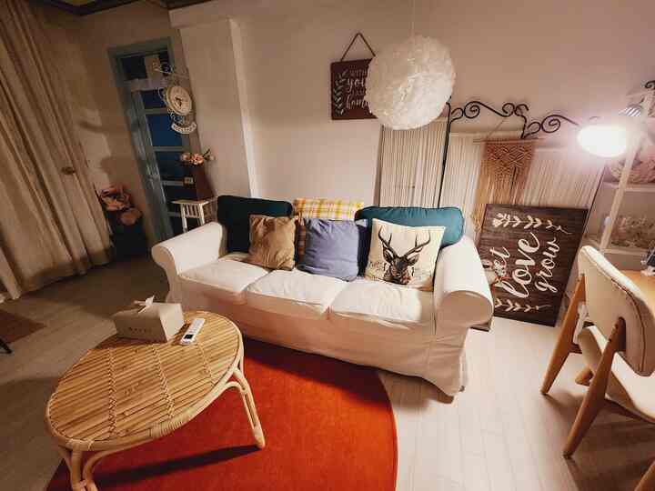 Warm wood tones and white living room featuring a 3-seater sofa with colorful cushions, rattan coffee table, and an orange rug in a cozy vintage style
