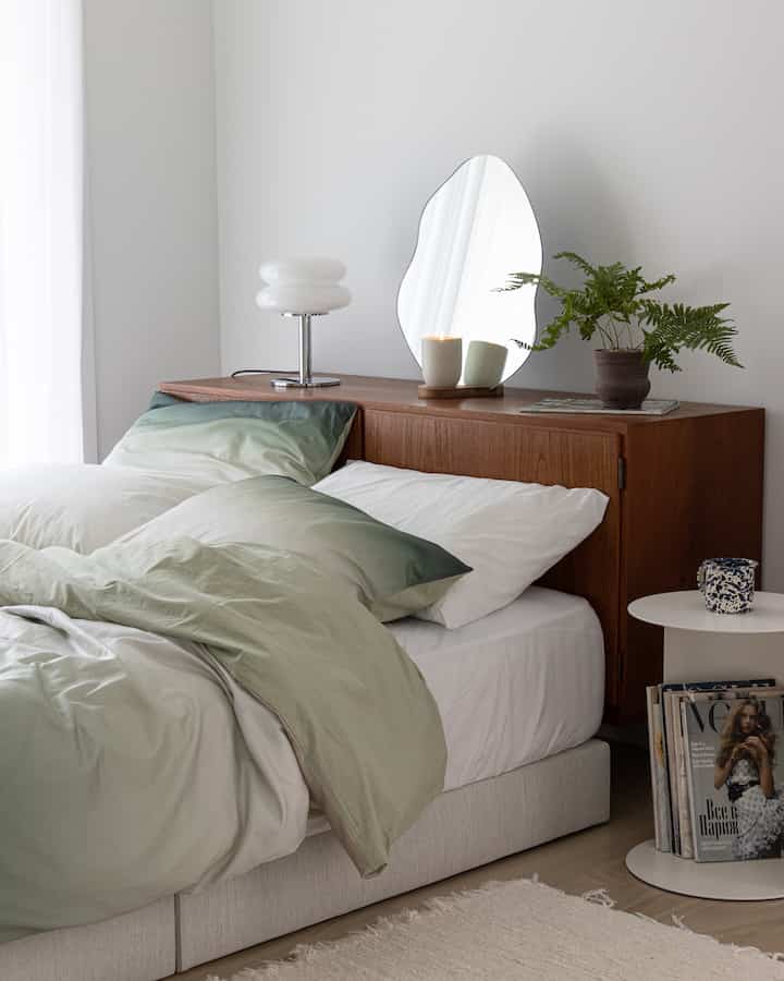 A natural-toned bedroom featuring a wooden sideboard with an irregular mirror and table lamp, creating a cozy atmosphere