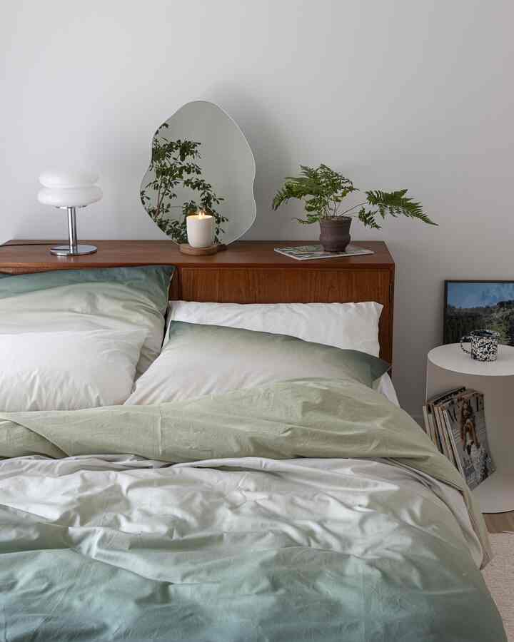 ナチュラルなグリーンと木目調が調和する寝室、植物と有機的な形の鏡が配置された落ち着いた雰囲気のインテリア