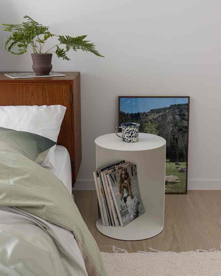 White-walled bedroom with wood tone bed, featuring a nightstand with a mug and a poster arranged for a warm atmosphere