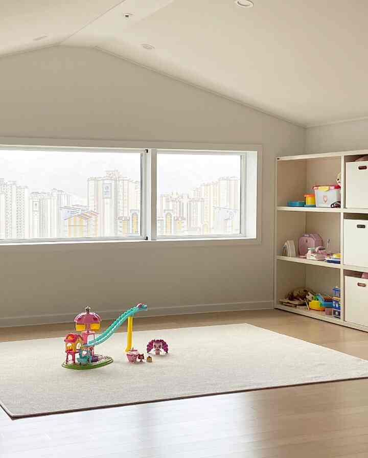 明るいベージュとホワイトの色調の子供部屋、中央のラグの上におもちゃがあり、右の壁には本棚が配置された整った空間