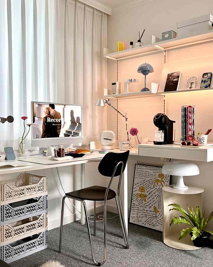 White-toned home office featuring a computer desk, black office chair, coffee machine, and plant creating a cozy work environment