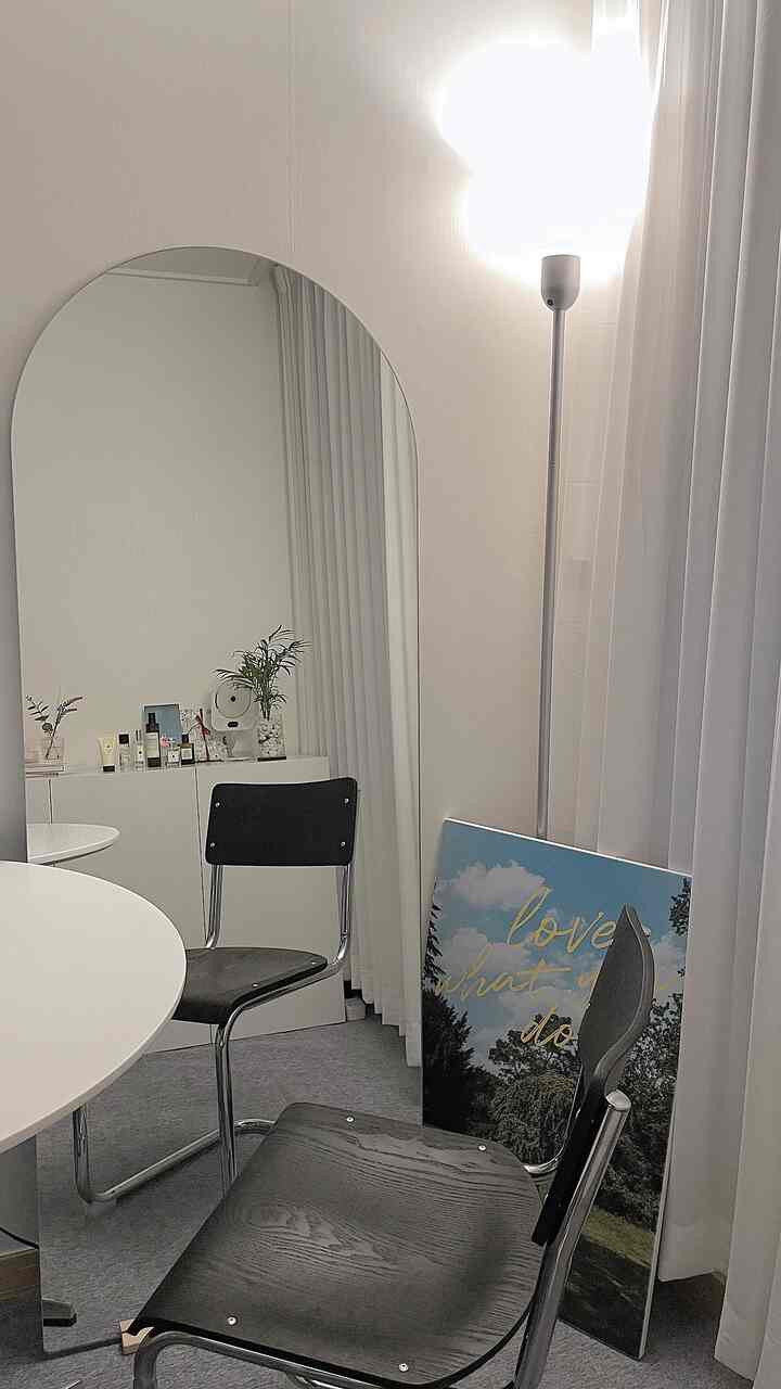 Small space in white and black tones featuring a round dining table, chairs, arched mirror, and floor lamp for a simple modern vibe