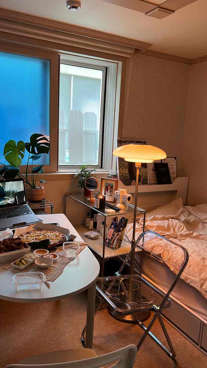A cozy small bedroom in white and beige tones featuring a transparent folding chair and floor lamp in a single household setting