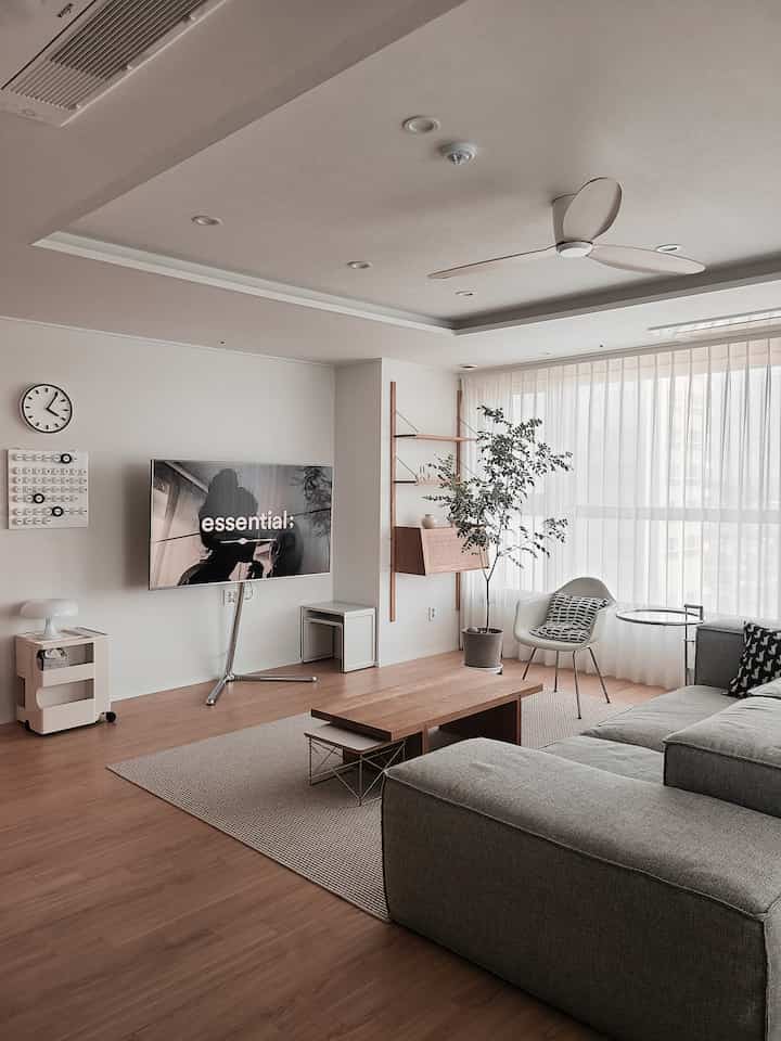 グレーのソファと木目調の床、テレビスタンドが配置されたモダンでナチュラルな印象のリビング