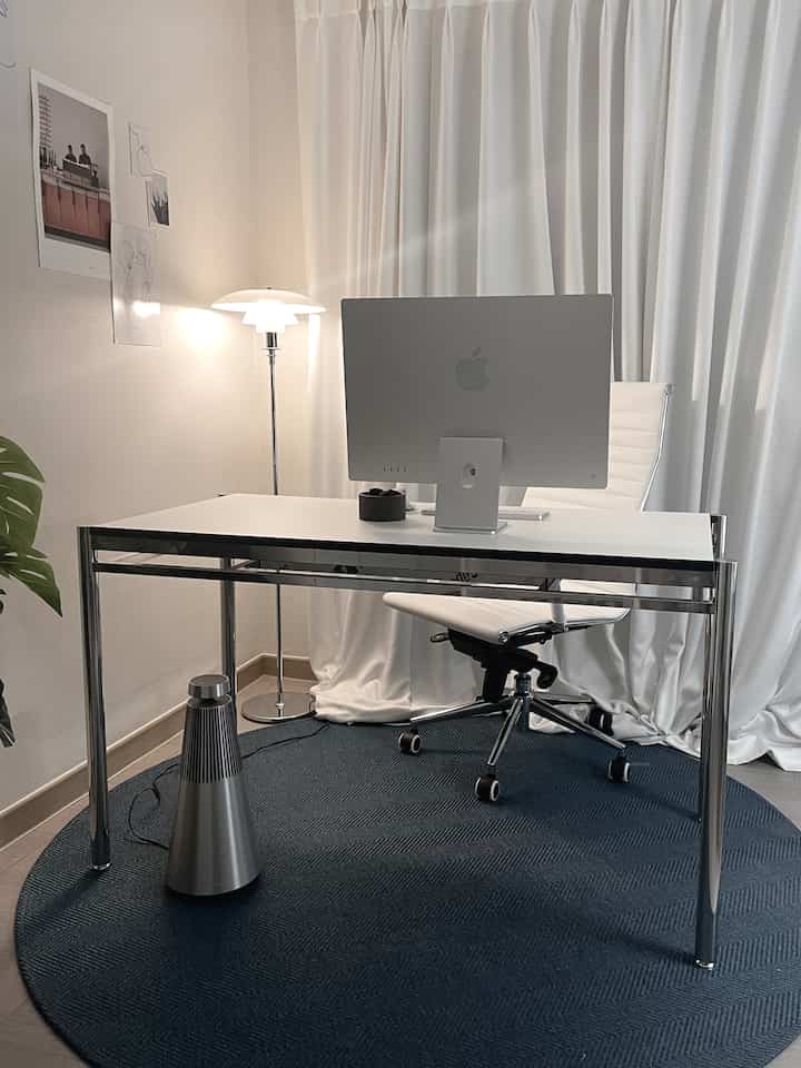 白とネイビーのトーンのミッドセンチュリーモダンなホームオフィス、白いデスクとチェア、ラウンドラグとフロアランプが配置された清潔感のある作業空間