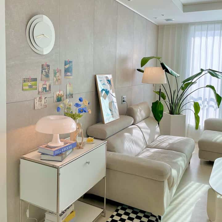 明るい白とベージュ色調のリビング、ソファやフロアランプ、カーテンが配置された雰囲気のあるインテリア。