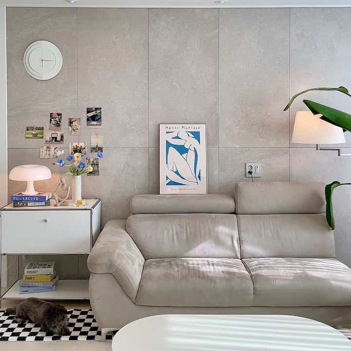 Beige and white toned living room featuring beige sofa, wall clock, side table, and floor lamp in a calm atmosphere
