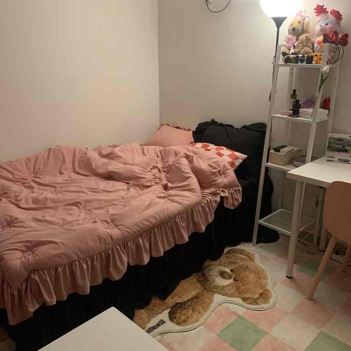 ピンクと黒の色調が調和する一人暮らしの寝室、ベッド、デスク、テディベアのラグが配置された落ち着いた雰囲気の空間