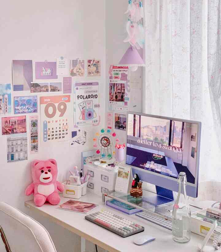 White and pink toned compact home office space featuring an organized desk, monitor, and a pink stuffed bear with a simple aesthetic
