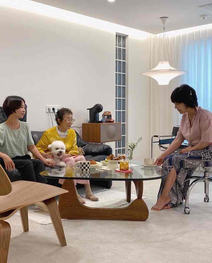 A white and wood-toned living room featuring black leather armchairs, a wooden coffee table, and a cozy setting with a dog and people.