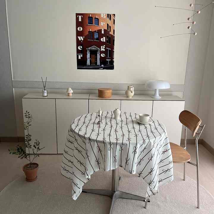 白とナチュラルウッド調のダイニング、丸いテーブルに模様のテーブルクロスとシンプルな収納が配置された雰囲気のある空間