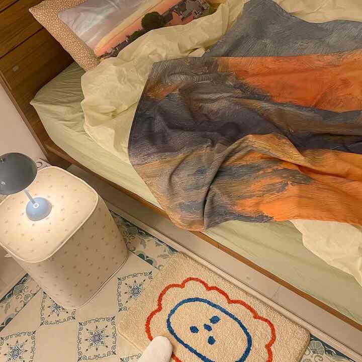 Natural-toned bedroom featuring a wood frame bed with colorful duvet cover, cozy rug and stool creating a warm atmosphere