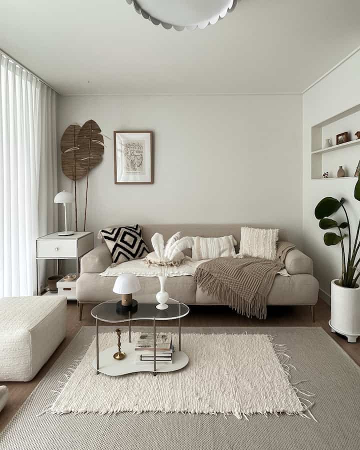 Bright white and beige toned living room featuring a beige sofa with cushions, a rug and small table in front, natural modern style space