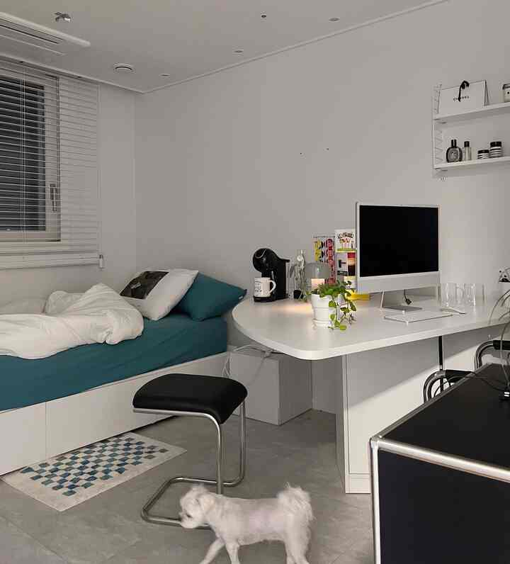 ホワイトトーンの一人暮らし用の小さな寝室、モダンなデスクとコーヒーマシンが配置された雰囲気のある空間