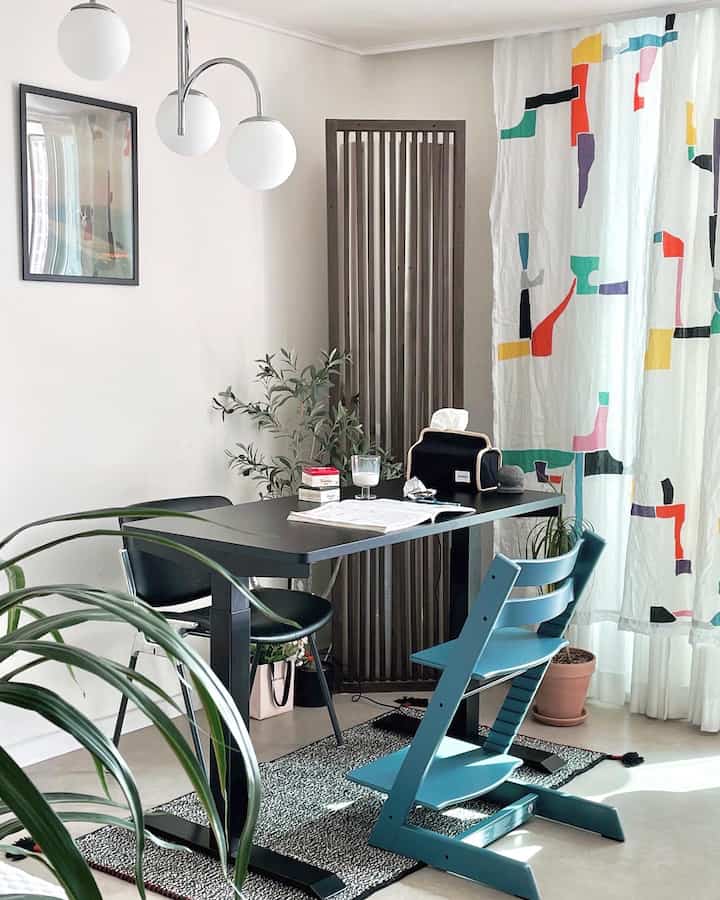 A modern dining room in white and black tones featuring a blue chair and plants in a study space