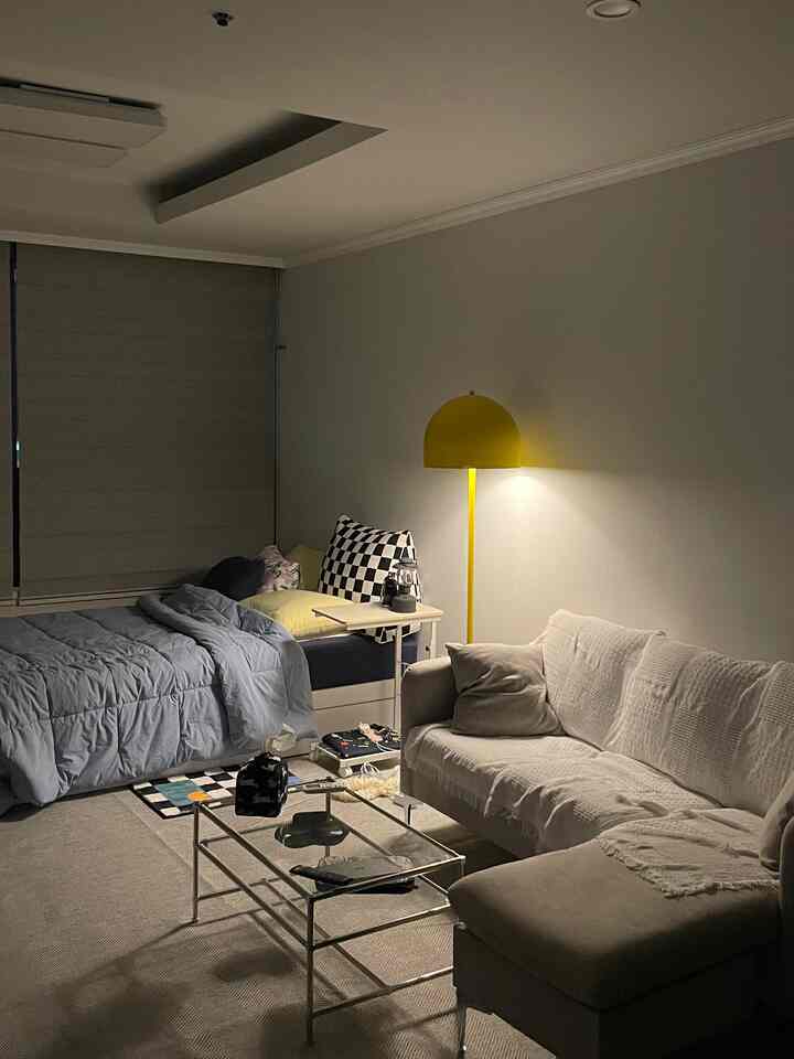 Neutral-toned small studio living and bedroom with beige sofa and yellow floor lamp, creating a cozy atmosphere