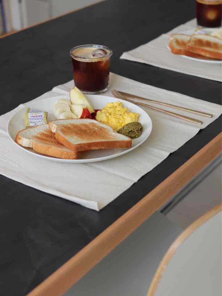 Warm brown and beige toned dining table featuring a plate of toast, scrambled eggs, fruit, and a glass of iced coffee creating a cozy breakfast setting