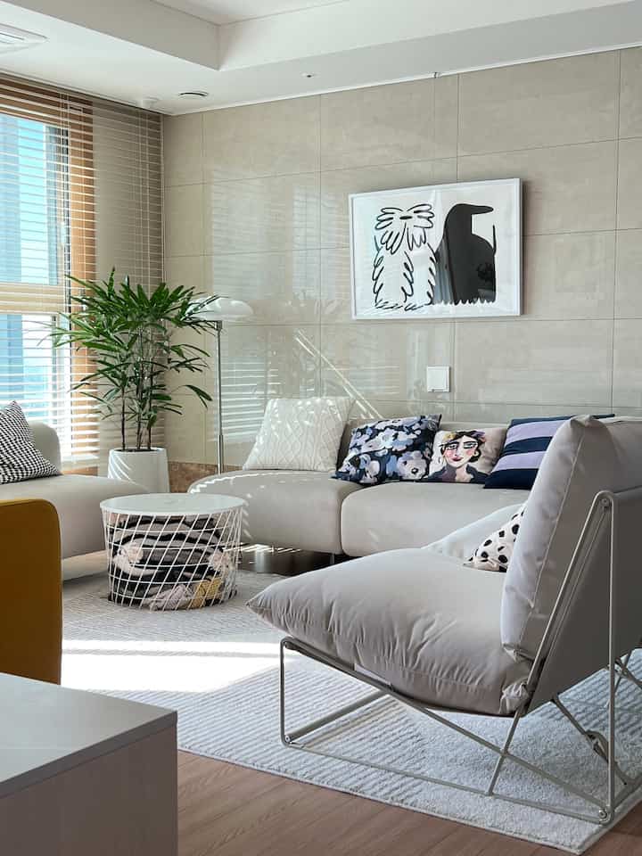 ホワイトとベージュの色調のリビング、ナチュラルなソファとブラインド、額縁が調和し明るく自然な雰囲気のあるインテリア