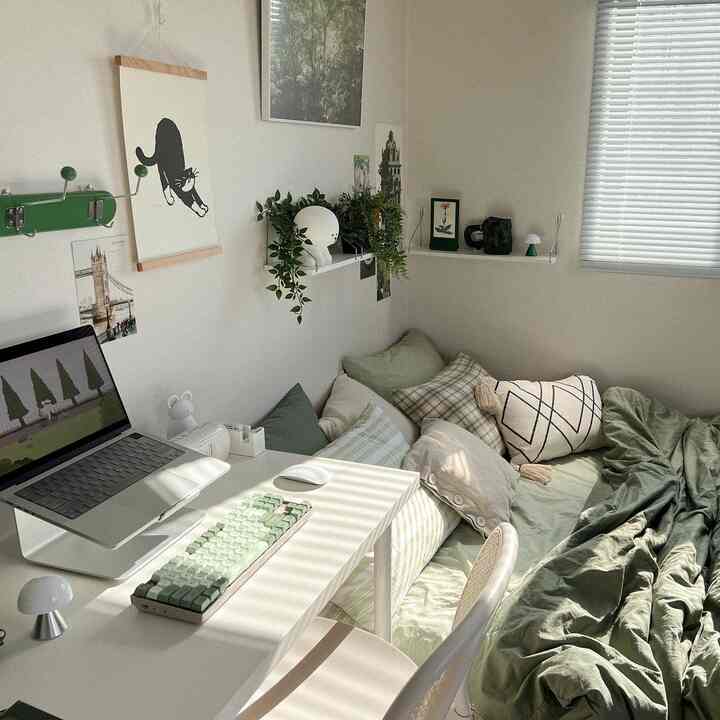 A small bedroom in white and green tones featuring a compact desk and cozy bedding with a simple, natural atmosphere