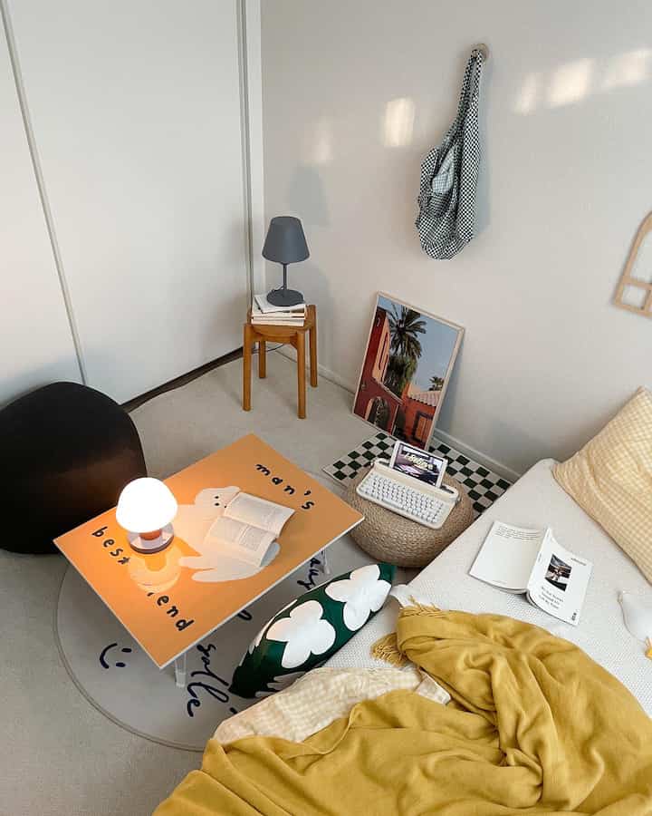A cozy small room in yellow and white tones featuring a picture frame table and a wooden stool