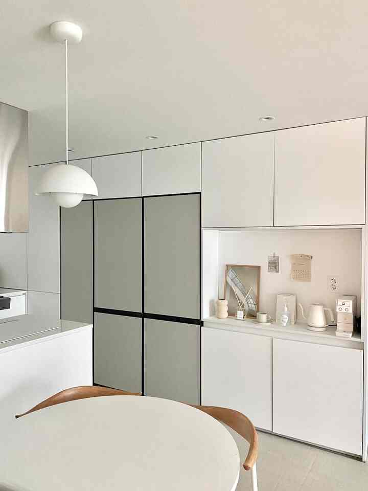Modern kitchen space dominated by bright white and gray tones, featuring built-in wall storage, two bespoke refrigerators, and home cafe accessories for a clean look.