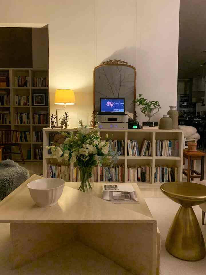 White and gold-toned living room featuring a central bookshelf and ornate gold-framed mirror, creating a cozy atmosphere