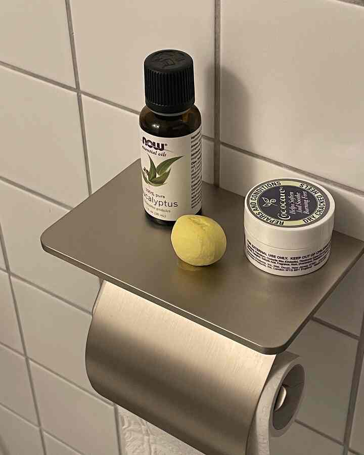 Silver towel rack shelf mounted against white tiled wall featuring a bottle of oil and moisturizing cream in a bathroom setting
