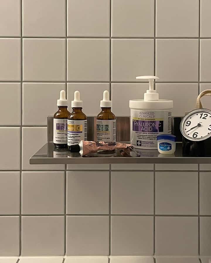 Bathroom space with white tiled wall and metal shelf displaying skincare products and a small clock