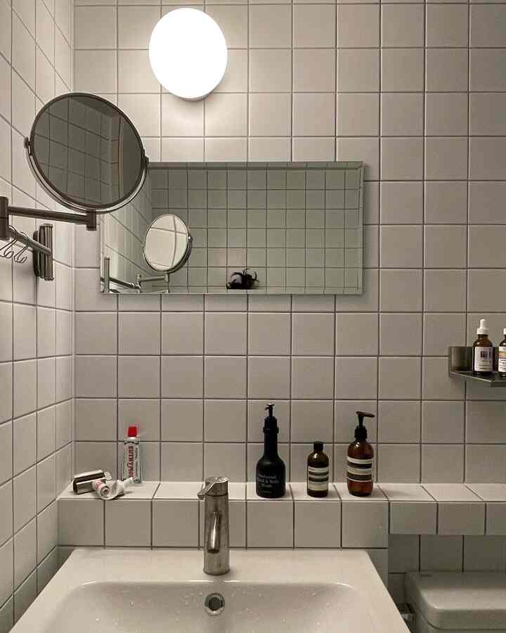 Clean white tiled bathroom featuring IKEA articulating mirror and rectangular wall mirror in a practical setting