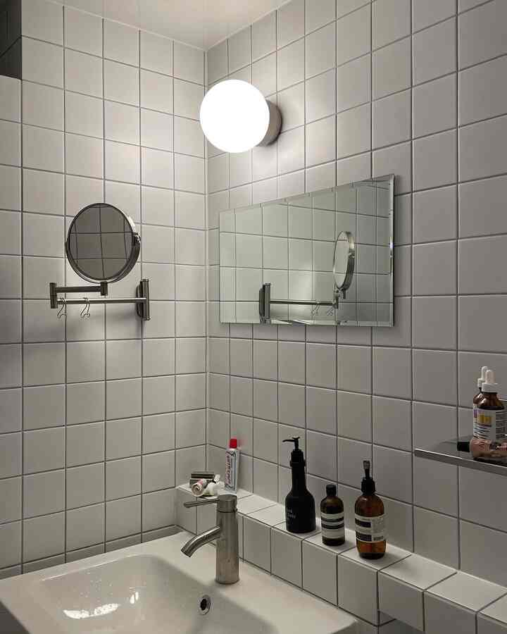 White-tone bathroom featuring tiled walls, sink, round and rectangular mirrors in a modern space