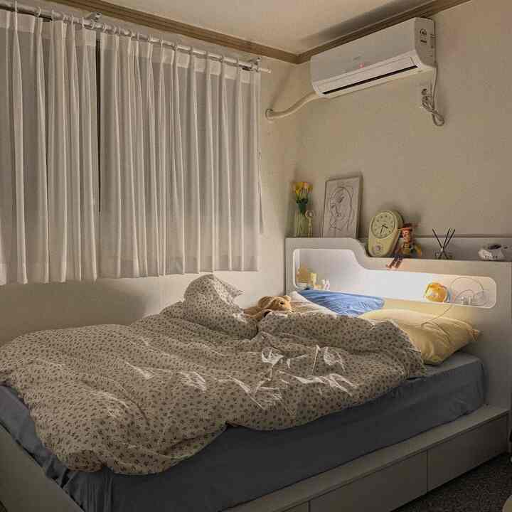 A bedroom with white walls and curtains, blue bedding, featuring a teddy bear and Toy Story toys as cozy accents