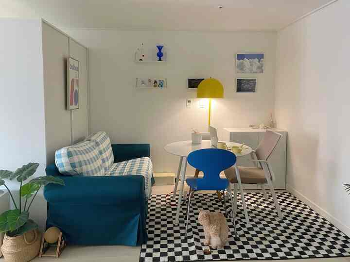 ホワイトトーンの壁にブルーのソファ、丸テーブルと黄色のフロアランプが配置された印象的なリビングスペース