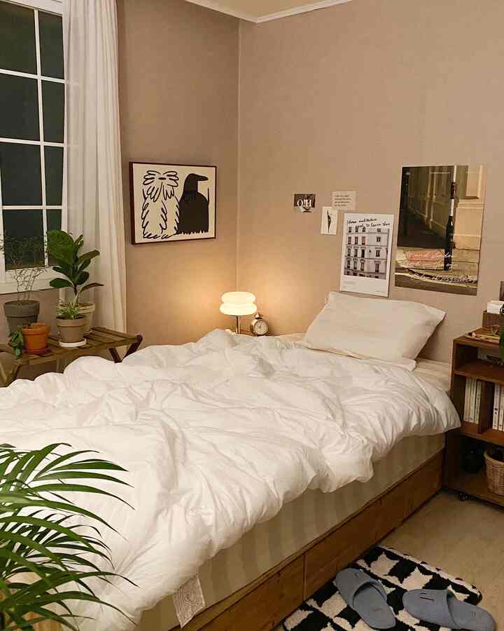Cozy studio bedroom with white bedding, natural wood furniture and warm brown walls creating a serene atmosphere